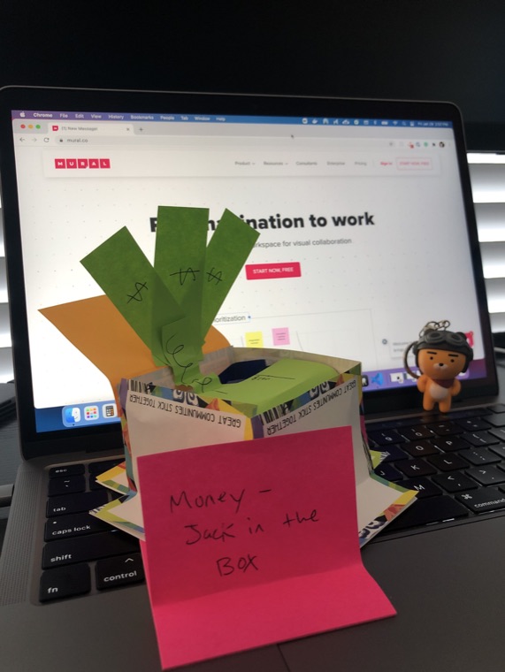 A paper prototype standing in front of a laptop, with a pink sticky note attached.